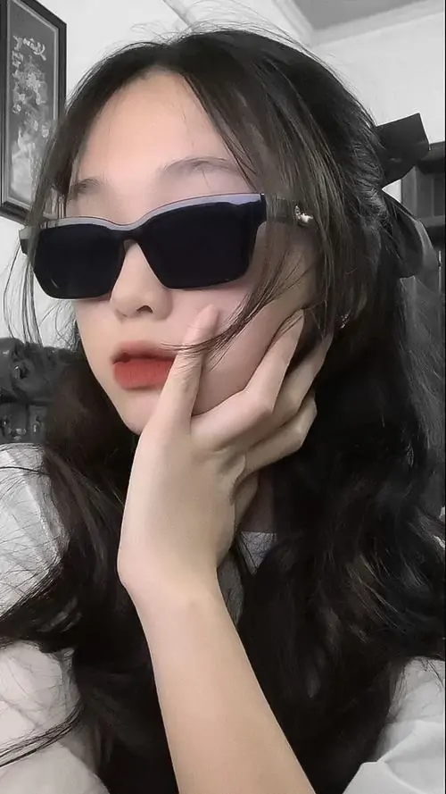 24 Gái đẹp đeo kính đen chụp cận mặt trên nền sáng xanh, tóc dài buông nhẹ và bàn tay chạm má tạo dáng rất tự nhiên, bức ảnh thiên về vẻ chất riêng, gọn gàng và hợp kiểu ngắm nhanh là thấy thu hút
