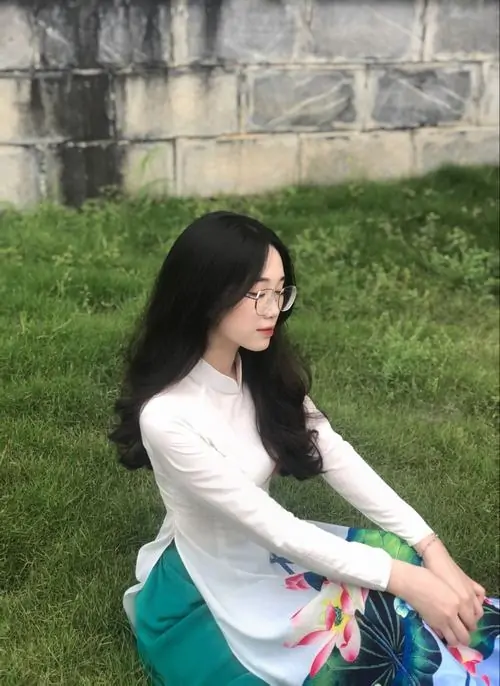 25 Hình cô gái ngồi ngoài bãi cỏ với áo dài tay màu kem và váy xanh, mái tóc đen suôn chảy sau vai, cô nàng đeo kính nhìn nghiêng dịu dàng, khung cảnh sân vườn làm bức ảnh trở nên mát mắt và êm ái
