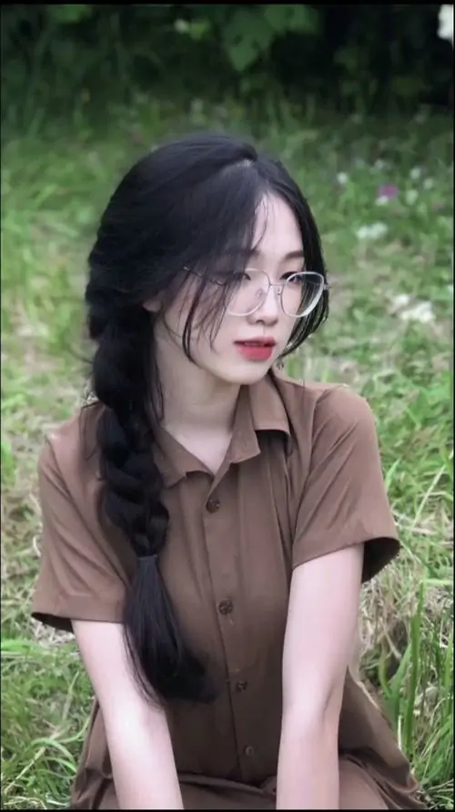 26 Nàng thơ đeo kính mặc áo nâu ngồi giữa nền lá xanh, tóc tết lệch mềm và tư thế khép tay phía trước tạo cảm giác ngoan hiền, nét nữ tính hòa với vẻ ngầu nhẹ khiến bức hình rất duyên và dễ mến