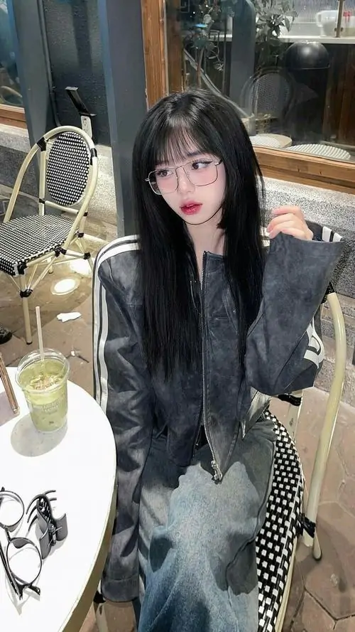 3 Hình gái đẹp trong bộ đồ tối màu đứng cạnh bàn với ly nước và món tráng miệng, mái tóc dài ôm gương mặt, ánh mắt nhìn thẳng tạo cảm giác dịu mà hút, khung cảnh quán xá khiến bức hình thêm gần gũi