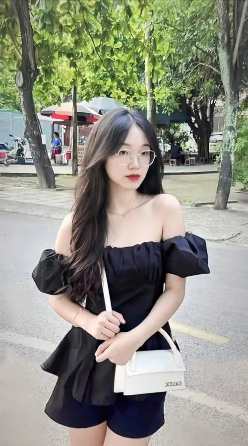 4 Cô nàng đeo kính cá tính diện váy đen trễ vai đứng giữa con đường rợp cây, tay cầm túi nhỏ và dáng đứng gọn gàng, nét cuốn hút đến từ vẻ xinh xắn tự nhiên cùng nhịp ảnh ngoài phố đầy sức sống