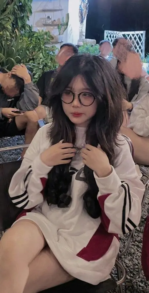 6 Nàng thơ đeo kính cá tính ngồi giữa đám đông với mái tóc xõa rối nhẹ, áo tông trung tính và biểu cảm bối rối đáng yêu, bức ảnh ghi lại phút tự nhiên rất đời, vừa mềm mại vừa có chút bí ẩn dễ mến