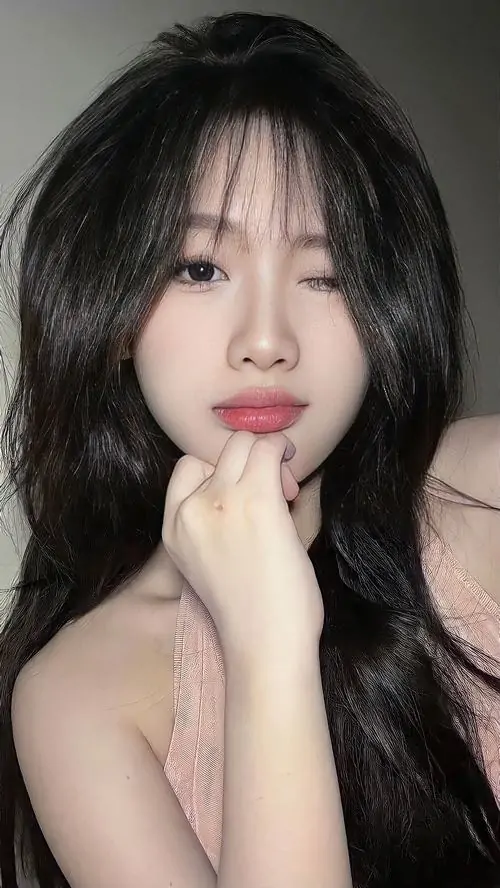 12 Cô gái tóc đen dài, vai trần và tay đặt hờ bên cằm, chụp cận trước nền tối mềm, mang đến bộ ảnh người đẹp nổi bật toàn cầu cảm giác nữ tính sâu lắng với gương mặt hài hòa và nụ cười mềm và sáng