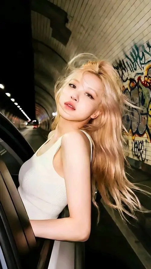 20 Cô gái tóc vàng xoã dài, áo trắng ôm dáng và người nghiêng về trước giữa nền tối có lá cây, tạo cảm giác ảnh người đẹp nổi bật toàn cầu khá bốc lửa nhưng vẫn dễ thương theo kiểu rạng rỡ, tươi và đầy sức sống