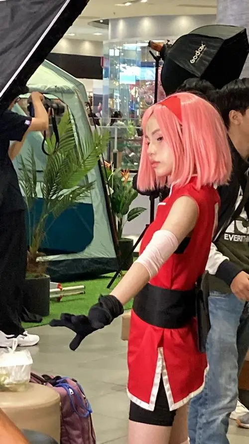 5 Ảnh coser nữ Việt hóa thân nhân vật tóc hồng với bodysuit đỏ đen găng tay dài và dáng quay nghiêng bên quầy trưng bày