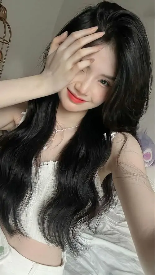 12 Bức selfie che nửa mặt bằng bàn tay làm điểm nhìn dồn vào tóc đen uốn sóng và áo trắng ôm dáng, tổng thể nghiêng về poker face hiện đại, vừa quyến rũ vừa giữ độ xa cách đúng kiểu ảnh cô gái bí ẩn