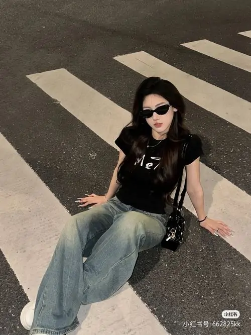 22 Trên vạch qua đường, cô gái đeo kính râm, mặc áo đen ngắn và quần jeans rộng, tư thế ngồi thả lỏng làm nổi rõ phong cách Streetwear, cả bức toát lên sự tự chủ cùng nét ngầu rất thành thị