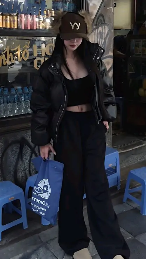 23 Hình nàng đứng trong không gian quán tối, đội mũ đen và mặc nguyên cây đen ôm dáng, tay xách túi xanh tạo điểm nhấn tương phản, đây là kiểu ảnh nữ ngầu có khí chất im lặng nhưng vẫn rất bắt mắt