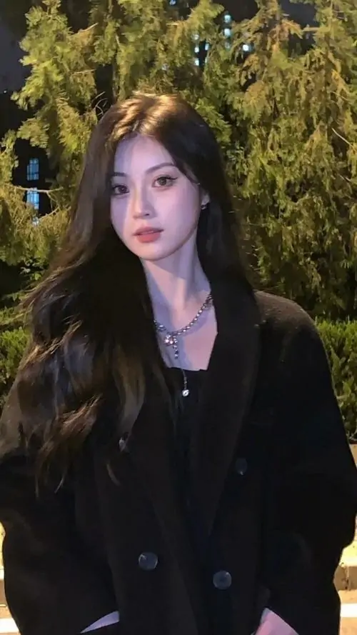 26 Giữa nền cây tối, cô gái mặc blazer đen, đứng thẳng và để tóc rơi tự nhiên quanh mặt, khung hình giống ảnh chân dung cá tính vì nhấn vào dáng đứng gọn, vẻ sắc sảo và sự tối giản không cần nhiều phụ kiện