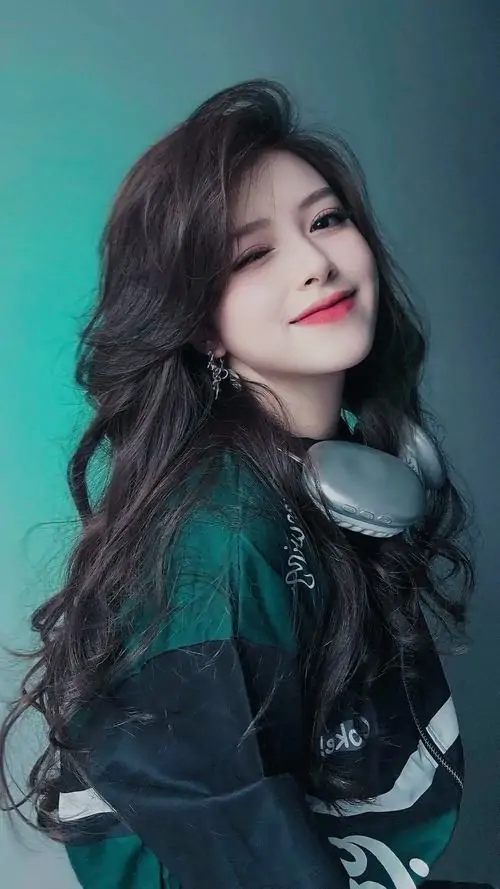 27 Hình thiếu nữ chụp studio với mái tóc xoăn dày, tai nghe đặt ở cổ và áo xanh sẫm, nụ cười nhẹ làm bức này mềm hơn nhưng vẫn giữ cá tính mạnh nhờ nền màu trơn và cách hất cằm rất có lực