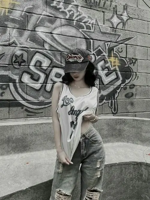 4 Khung hình đơn sắc bắt trọn cô gái đứng trước mảng tường graffiti, áo sáng và quần rộng làm tổng thể giống ảnh đen trắng nghệ thuật, vẻ đẹp sắc lạnh hiện lên qua cách cúi mặt nhẹ và không gian đường phố có độ bụi