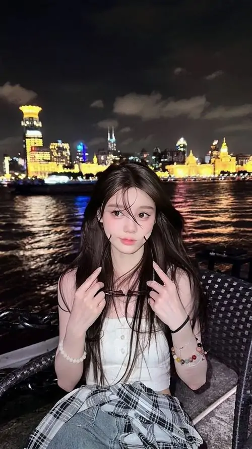5 Ảnh nữ chụp buổi tối bên sông, phía xa là đèn thành phố phản chiếu mặt nước, cô gái giơ tay tạo dáng vui mắt nhưng vẫn giữ thần thái cuốn hút nhờ mái tóc dài, áo hở vai và sắc đêm rất sâu