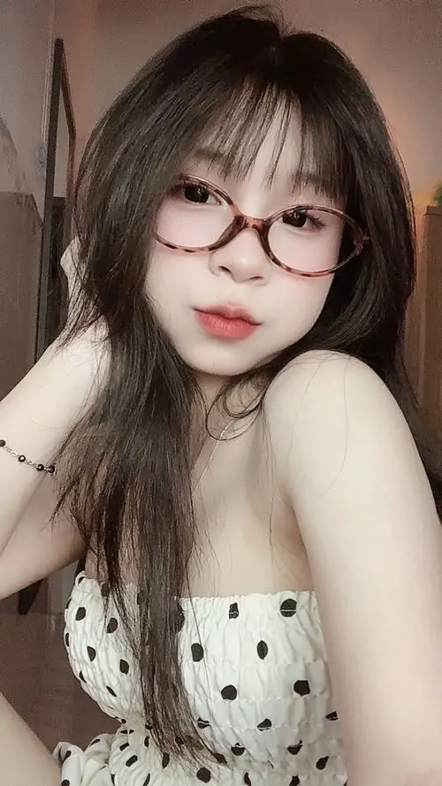 8 Gương mặt đeo kính tròn, tóc xõa rối nhẹ và áo chấm bi sáng màu giúp bức này giống ảnh chân dung cá tính theo hướng mềm mà không nhạt, nổi bật nhất là môi hờ khép và ánh nhìn thẳng đầy tự tin