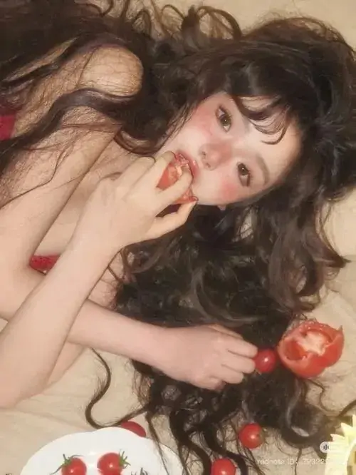 14 Mái tóc đen xõa rộng, người mẫu nằm giữa táo đỏ và nền vải nhạt, khung ảnh tạo đối lập ngọt và tối rất rõ, nhiếp ảnh hình thể dùng sắc đỏ để nhấn chiều sâu cảm xúc mà không làm mất vẻ tự nhiên