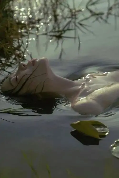 24 Mặt nước đục nhẹ ôm lấy người mẫu đang nổi nghiêng, một cành cây mảnh kéo mắt nhìn theo thân người kéo dài, nhiếp ảnh hình thể khai thác vẻ mộc và nhân văn, khiến khung hình giống một giấc mơ chậm