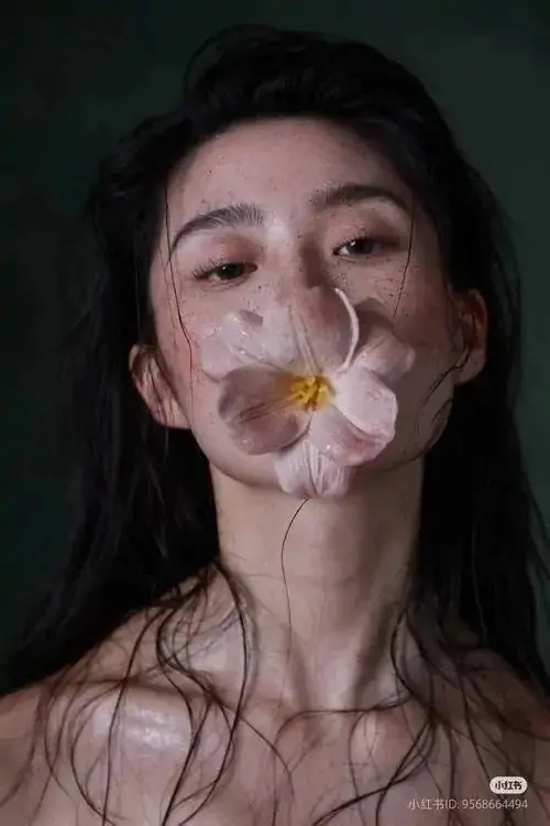 26 Chân dung cận mặt ghi khoảnh khắc người mẫu ngậm cánh hoa, tóc đen ướt phủ qua má và cổ, ảnh khỏa thân nghệ thuật thiên về cảm giác hơn phô bày, giữ nét tinh tế và sắc thái rất lạ, rất cuốn