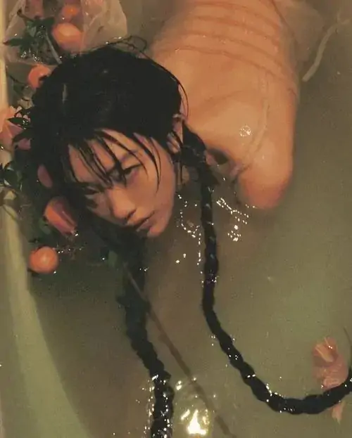 28 Góc chụp nàng thơ bắt cận gương mặt cùng cánh tay đưa cao, mái tóc ướt quấn thành bím dài trên nền nâu ấm, ảnh khỏa thân thẩm mỹ chú trọng chất da, hơi nước và nhịp thân thể đầy bản năng mà vẫn sang