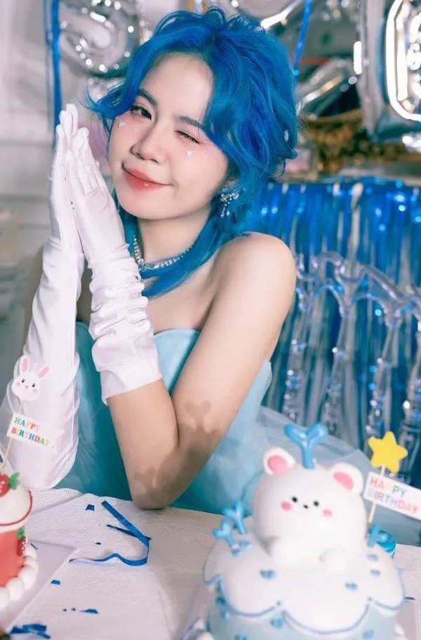 Simmy ngồi ngoài trời tóc xanh bay nhẹ nụ cười rạng rỡ tôn gò má và làn da mịn