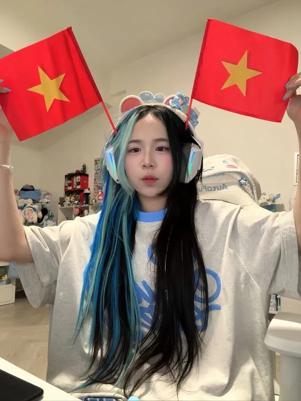 Simmy đứng trước cờ đỏ tạo dáng tự tin nhắc Hero Team mà vẫn giữ nét dịu dàng