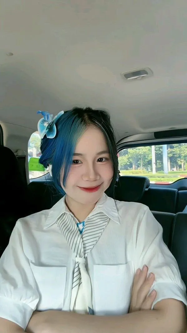 Simmy ngồi trong xe cười nhẹ tóc xanh buông dài tôn cổ thon và đôi vai mịn