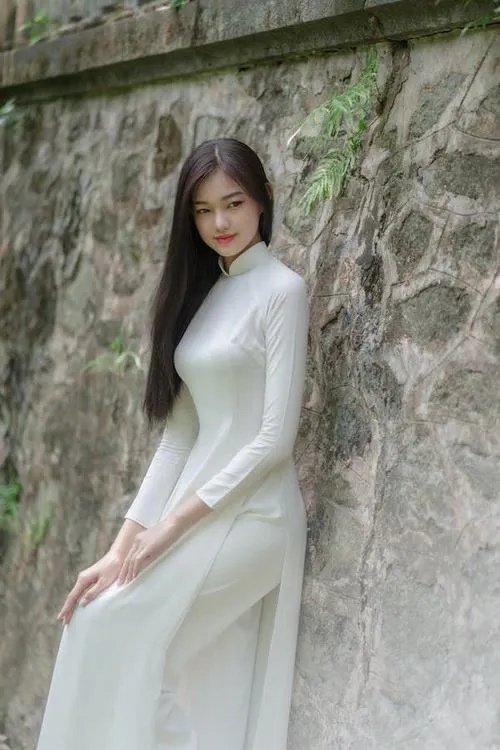 14 Nữ sinh trong áo dài trắng đứng cạnh bức tường đá mái tóc đen buông dài làm nổi bật khí chất thanh và yên