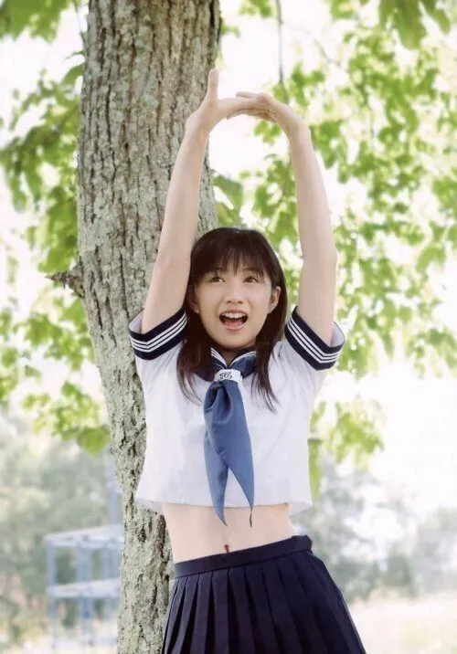 16 Cô nàng mặc áo trắng váy xanh giơ tay bên thân cây lớn mang vẻ hồn nhiên và năng động như buổi chơi đùa sau giờ học