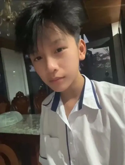 13 Ảnh nam sinh Gen Alpha ghi lại khoảnh khắc cậu bạn mặc sơ mi trắng đứng cạnh bàn, mái tóc hơi rối và mắt nhìn xuống tạo nét ngại ngùng tự nhiên, rất hợp chủ đề ảnh học sinh cute và vibe học đường