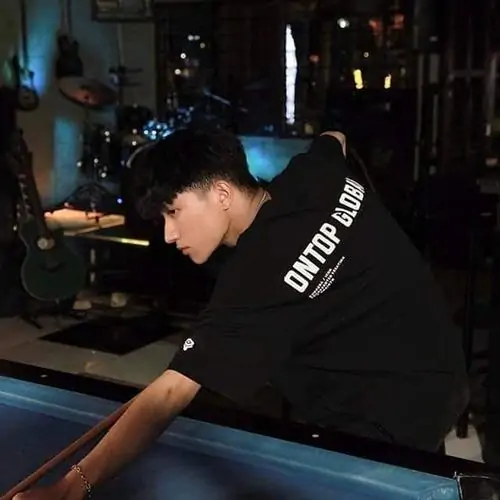 17 Ảnh bạn nam 2k12 ghi lại lúc cậu bé cúi người bên bàn bida trong không gian tối, áo đen làm khung ảnh mạnh hơn, dáng chụp tự nhiên gợi phong cách Gen Alpha hơi ngầu mà vẫn giữ nét trẻ trung