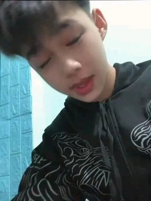 22 Bạn nam sinh 2012 trong hoodie đen ngồi nghiêng nhẹ giữa không gian kín, nét mặt bình thản và tay giữ dây áo tạo cảm giác tự nhiên, ảnh có vibe trong sáng nhưng vẫn đủ ngầu theo gu nam sinh aesthetic