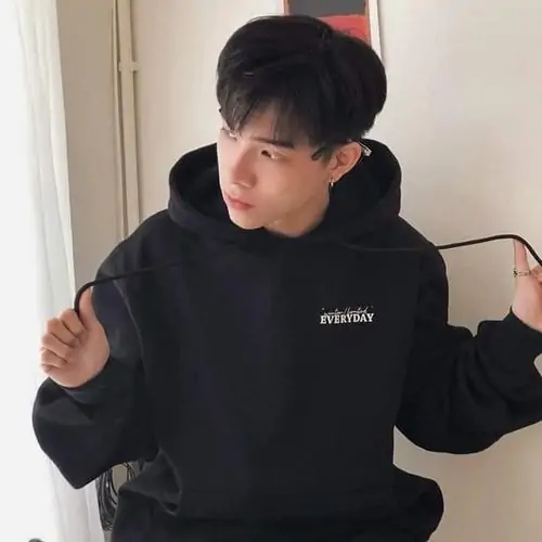 2 Cậu bạn 2012 mặc hoodie đen ngồi trong phòng, hai tay kéo nhẹ dây áo nhìn nghiêng khá ngầu nhưng vẫn dễ thương, khung hình gọn sạch gợi rõ phong cách học đường và nét tự nhiên đúng kiểu hot boy nhí