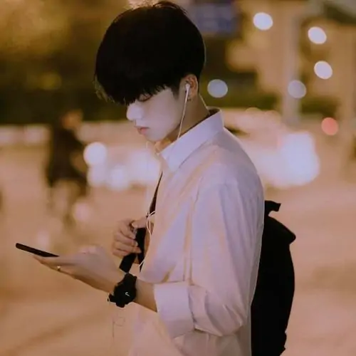 3 Hình nam sinh k12 đứng ngoài đường buổi tối với áo sáng màu, một tay cầm điện thoại như vừa xem tin nhắn, hậu cảnh đèn mờ giúp ảnh có màu ảnh sáng dịu và chút biểu cảm ngại ngùng rất hợp vibe trong trẻo