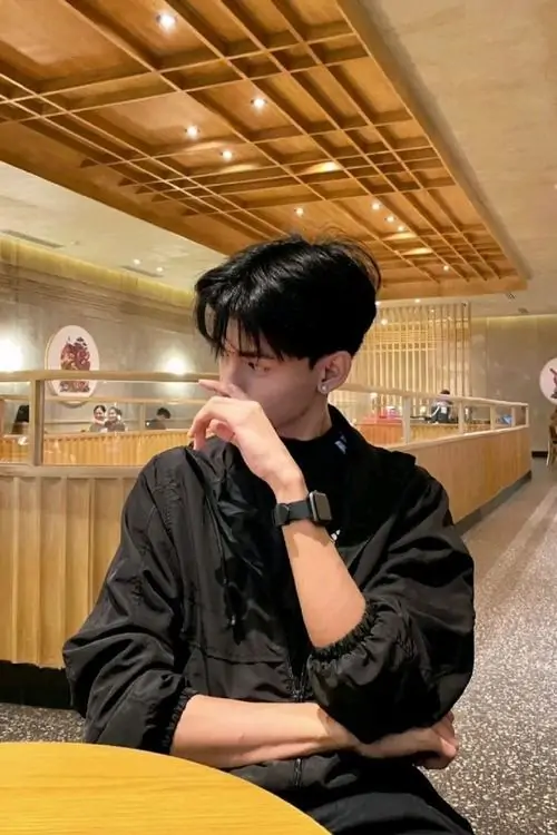 13 Ảnh cậu trai trong quán gỗ ấm màu, nghiêng mặt sang bên và dùng tay chống cằm che miệng, ánh đèn vàng làm đường nét mềm hơn nên nhìn cute, hợp kiểu ảnh trai đẹp che mặt ngầu nhưng vẫn gần gũi