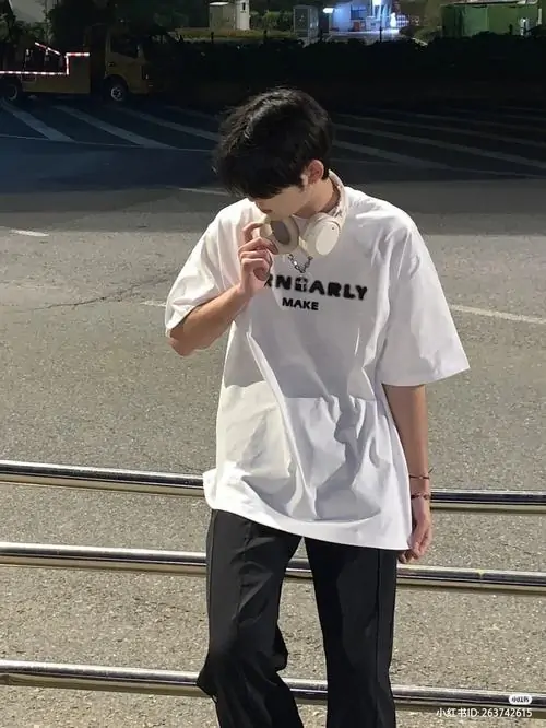 16 Cậu nam sinh mặc áo trắng đứng cạnh hàng rào đêm, giơ điện thoại ngang mặt để che mũi miệng, phần cổ và cánh tay lộ ra vừa đủ khiến tổng thể hấp dẫn, hợp phong cách đăng mạng xã hội