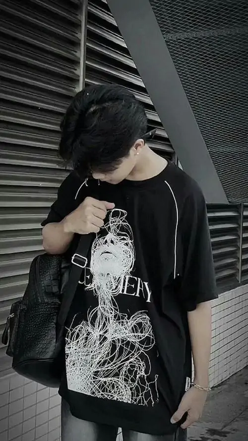 1 Ảnh trai mặc áo đen đứng trước mảng tường sọc, cúi nhẹ đầu và dùng điện thoại che nửa mặt, tay còn lại giữ túi trước ngực, tổng thể đẹp và lạnh, hợp kiểu ảnh trai ngầu giấu mặt mang thần thái bí ẩn