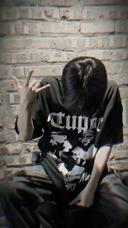 21 Ảnh trai đẹp mặc áo đen in chữ ngồi sát bức tường gạch, gập cổ xuống sâu để tóc buông trùm mặt, hai tay đặt gần đầu gối khiến tư thế thêm khép, bức ảnh nhìn hấp dẫn theo kiểu lạnh và bụi