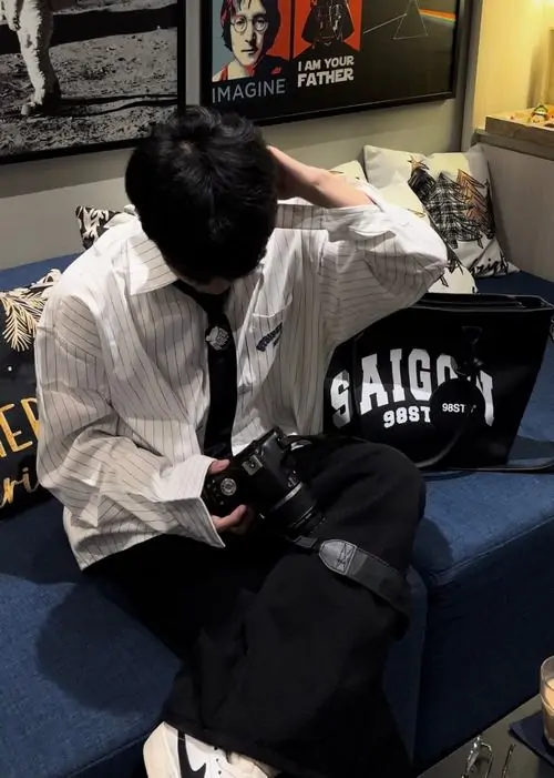 22 Cậu bạn áo sơ mi trắng thắt cà vạt ngồi trên giường, đưa tay lên vuốt tóc che trán và hạ mặt xuống thấp, ánh sáng phòng tối làm khung hình đẹp, gợi vẻ bí ẩn hơn là phô bày trực diện