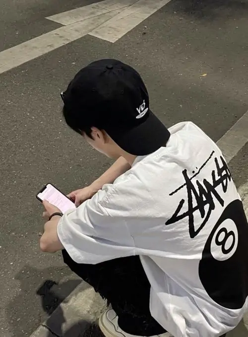 26 Từ góc chụp trên cao, chàng trai áo trắng đội nón đen cúi nhìn điện thoại nên vành nón che kín mắt, bờ vai tròn và tư thế thu mình tạo cảm giác lạnh, đúng kiểu ảnh trai ngầu giấu mặt hiện đại