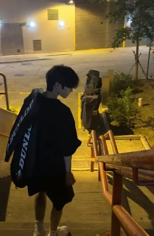 31 Ảnh trai mặc áo tối với dây chuyền bạc đứng sát vách kim loại, hơi cúi đầu và dùng điện thoại che phần mũi miệng, tóc rơi xuống trán làm bức hình có sức hút lạnh, hợp kiểu ảnh con trai giấu mặt chất