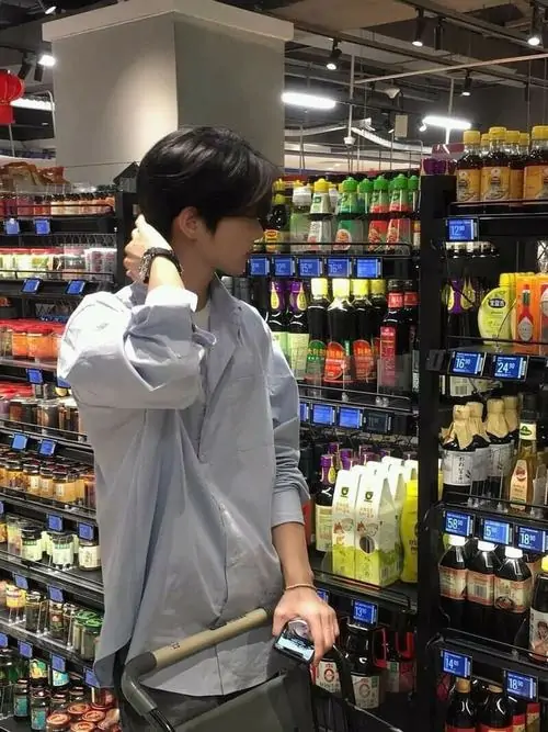 5 Ảnh nam thần trong cửa hàng tiện lợi dùng điện thoại áp sát mặt khi soi gương, tóc phủ nhẹ phần trán và cổ tay đeo đồng hồ làm điểm nhấn, khung hình sáng vừa đủ nên nhìn cute mà vẫn ngầu