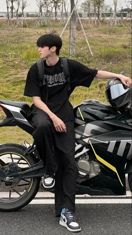 2 Chàng trai mặc nguyên cây đen ngồi trên xe máy bên đường vắng trong buổi chiều se lạnh dáng ngồi chắc và mắt nhìn xuống làm tổng thể toát ra vẻ nam tính rõ rệt hợp kiểu ảnh thời trang nam đầy phong độ