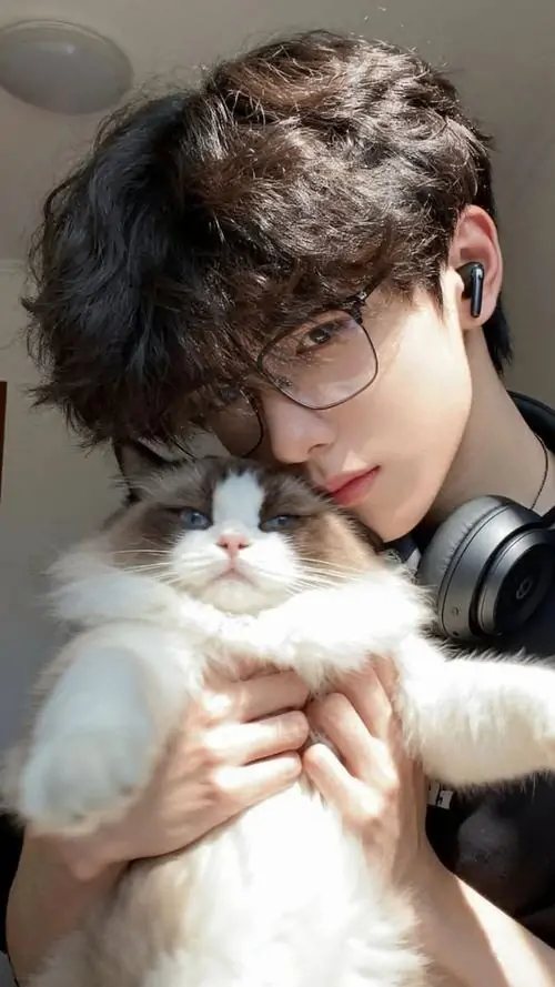 10 Hình chàng trai đeo kính ôm mèo trắng trước ngực, phần tai nghe đặt quanh cổ khiến khung hình có thêm chất đời thường, mái tóc rối nhẹ và biểu cảm dịu, ánh mắt sau kính tạo cảm giác ấm áp như một buổi tối ở nhà