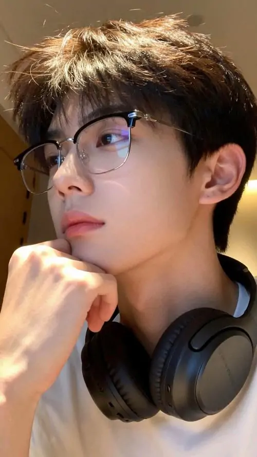 14 Ảnh nam thần kính cận ở góc bàn với tai nghe lớn quanh cổ, chàng trai chống cằm suy nghĩ trong ánh đèn vàng, khuôn mặt nghiêng nhẹ tạo cảm giác trưởng thành, gợi liên tưởng một học bá đang nghỉ giữa giờ học hoặc làm việc