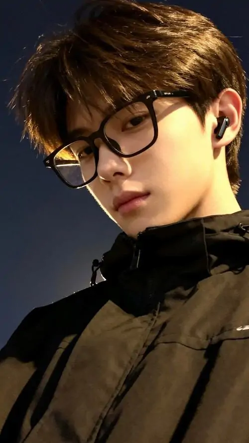 19 Bức bán thân chụp nghiêng với nền tối và ánh vàng xiên mặt, chàng trai mặc áo cổ cao tối màu, đường viền gọng kính nổi rõ, ảnh nam lạnh lùng được đẩy lên mạnh bằng biểu cảm kín, nhưng vẫn giữ sự thanh lịch nhờ gọng kính phù hợp