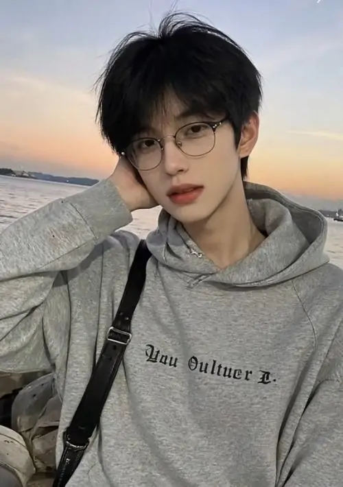 20 Ngồi trước nền trời chiều nhạt, chàng trai mặc hoodie xám và chống nhẹ đầu, gió làm tóc bay vừa phải, khung hình mang cảm giác thư giãn, sáng sủa và trẻ, đúng kiểu ảnh nam đẹp đeo kính dễ dùng cho ảnh đại diện