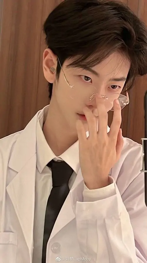 27 Ảnh trai xinh đeo kính trong sơ mi sáng màu và cà vạt đen, chàng trai đưa tay che nửa môi trước nền gỗ ấm, tạo cảm giác vừa chỉn chu vừa tinh nghịch, bức hình hợp nhóm người thích vẻ công sở nhưng không quá cứng