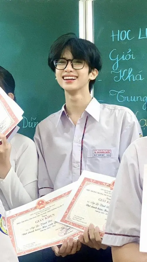 4 Khung hình học đường bắt trọn nam sinh mặc đồng phục đứng trước bảng, tay cầm giấy khen và mỉm cười nhẹ, ảnh trai đẹp học đường hiện rõ với sơ mi trắng gọn gàng, khí chất điềm đạm khiến bức ảnh sáng sủa và thiện cảm