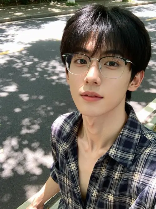 6 Chụp dưới tán cây loang nắng, chàng trai mặc sơ mi caro mở cổ, tóc rũ nhẹ và nhìn thẳng vào máy, kiểu gọng kính thanh mảnh tôn đường nét gương mặt, bầu không khí vừa lãng tử vừa có chút phong cách nghệ thuật rất rõ