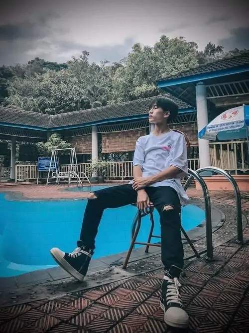 6 Hot boy 2010 ngồi ghế dài bên đường với cầm điện thoại selfie ánh mắt long lanh outfit xanh background con đường yên bình toát lên vibe tươi mới của Gen Alpha.