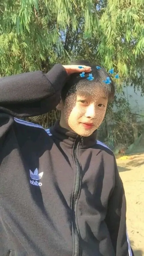 11 Khung hình nam sinh điển trai ngoài trời với áo khoác đen, một tay chạm đầu như chỉnh tóc giữa nền cây lá, ánh sáng mềm giúp gương mặt sáng hơn, rất hợp gu ảnh học sinh nam selfie theo kiểu gần gũi