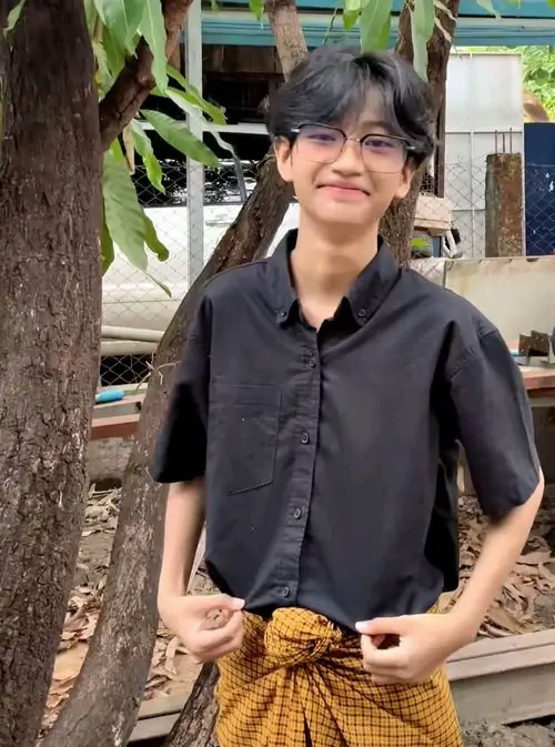 16 Một chàng trai k8 đứng cạnh thân cây, áo sơ mi đen phối quần vàng nâu tạo điểm nhìn lạ, nụ cười nhẹ và mái tóc hợp trend giúp bức ảnh mang vẻ thư sinh pha chút cá tính rất bắt mắt